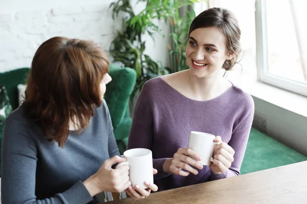Beautiful mature mother and her adult daughter are drinking coffee — Stock Photo, Image