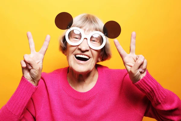 Anciana feliz mujer mostrando signo de victoria y mirando a la cámara —  Fotos de Stock