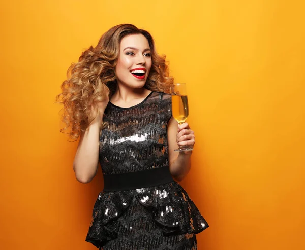 Schöne Mädchen in einem Cocktailkleid mit Abend-Make-up und Locken hält ein Glas Champagner — Stockfoto