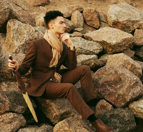 Jovem elegante sentado nas rochas perto do mar — Fotografia de Stock