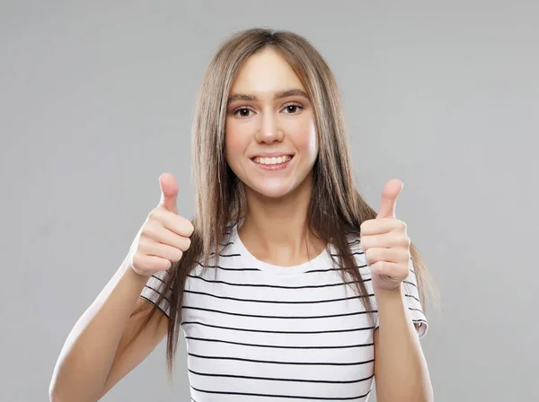 Happy young caucasian female making thumb up sign and smiling cheerfully, showing her support and respect to someone.