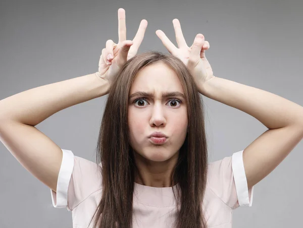 Smiling girl with raised hands holding  fingers as antlers on head — Stock Photo, Image