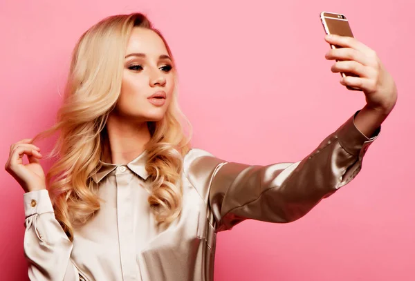Portrait de femme blonde souriante beautifu en vêtements décontractés avec un maquillage parfait avec smartphone, fait selfie sur fond rose — Photo