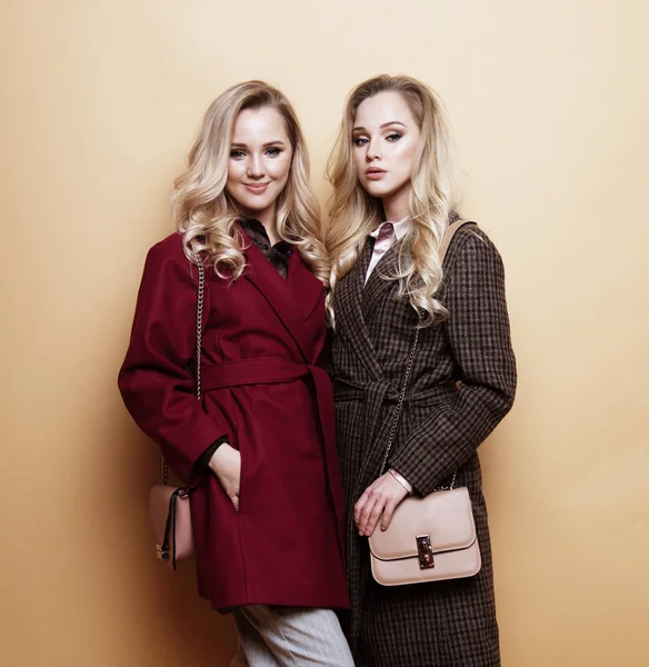 Модный портрет двух девушек, лучшие друзья позируют в помещении на бежевом фоне в зимнем стильном пальто. — стоковое фото
