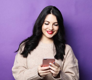 Uzun saçlı genç bir kadın, modern cep telefonunu tutuyor.