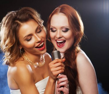 lifestyle, party and people concept - two beautiful stylish girls singing karaoke at the club clipart