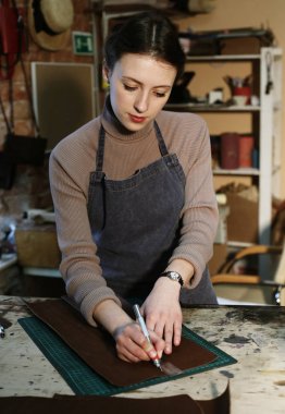 Genç bir kadın bir çanta stüdyosunda çalışıyor. Detayları çıkartıyor.