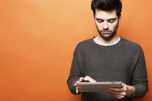 Hombre barbudo joven serio usando tableta digital contra fondo naranja — Foto de Stock