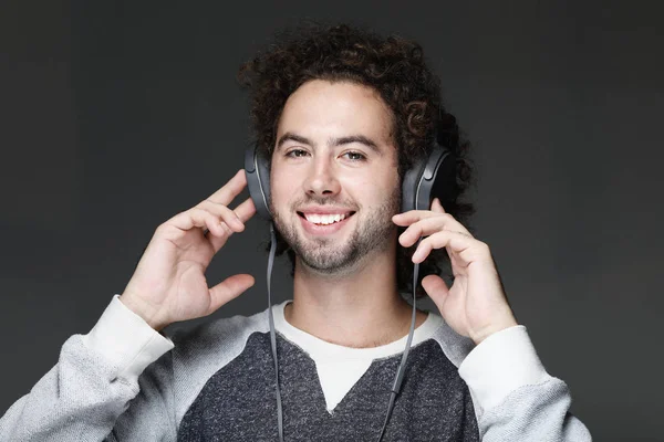 Χαρούμενος νεαρός χαμογελαστό να ακούτε μουσική στα ακουστικά. Σε γκρι φόντο. — Φωτογραφία Αρχείου