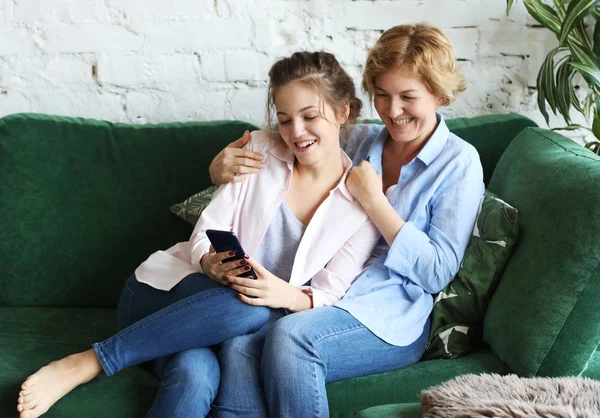 Familie, mennesker og teknologi. Aldret kvinne og hennes voksne datter bruker smarttelefon hjemme – stockfoto