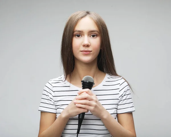 Девушка-модель певица с микрофоном на светло-сером фоне — стоковое фото