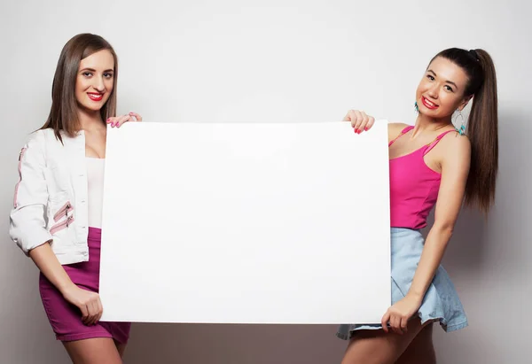 Образ жизни, эмоции и концепция людей: две юные подруги стоят вместе и держат пустой рекламный щит — стоковое фото