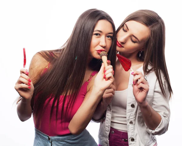 Portrait of two young pretty hipster girls holding candys. Studio portrait of two cheerful best friends having fun and making funny faces — Stock Photo, Image