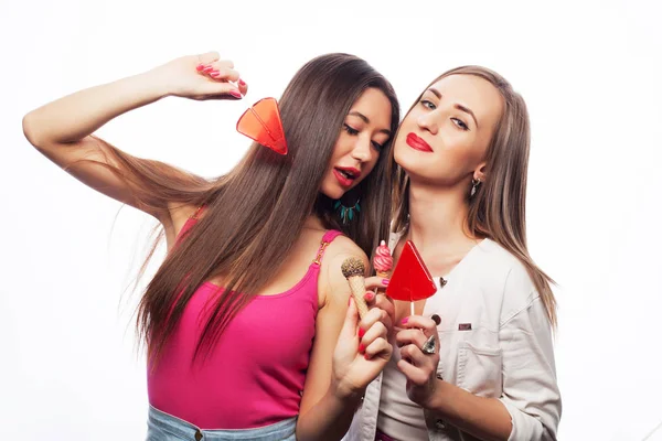 Portret van twee jonge mooie hipster meisjes houden Candys. Studio portret van twee vrolijke beste vrienden met plezier en het maken van grappige gezichten — Stockfoto