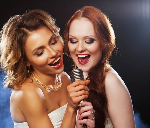 Estilo de vida, fiesta y el concepto de la gente - dos hermosas chicas elegantes cantando karaoke en el club —  Fotos de Stock