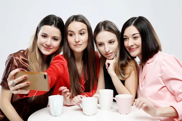 Amistad, personas, fiesta de pijama y concepto de tecnología - amigos felices o adolescentes con teléfono inteligente tomando selfie sobre fondo blanco —  Fotos de Stock