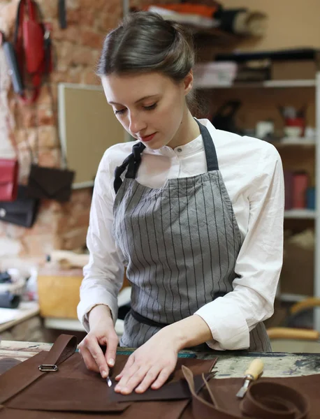 Молодая женщина работает в мастерской по изготовлению сумок, вырезает детали — стоковое фото