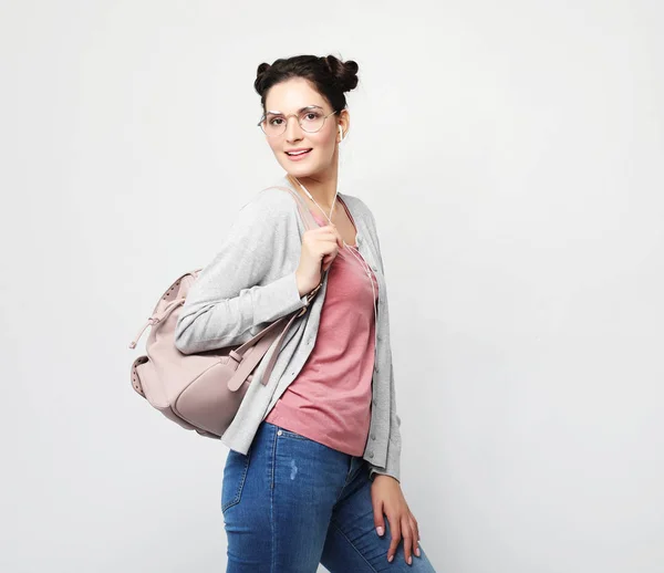 Young brunette woman wearing a pink t-shirt and jeans is holding a backpack and smiling — Stock Photo, Image