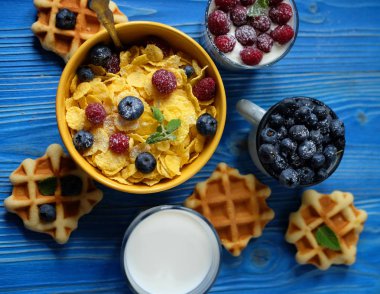 Sağlıklı kahvaltı. Ahududu ve yaban mersini, çilek, gofret ve süt ve yoğurt ile granola ile Mısır gevreği.