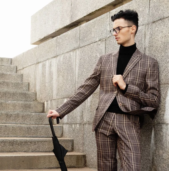 Elegantní mladý muž v brýlích s deštníkem stojící na schodech — Stock fotografie