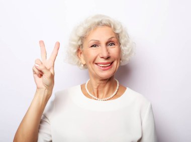 Yaşlı kadın gülüyor ve barış ya da zafer işareti gösteriyor. Duygular ve duygular. Anlamlı büyükannenin portresi..