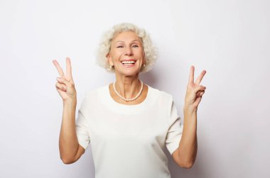 Yaşlı kadın gülüyor ve barış ya da zafer işareti gösteriyor. Duygular ve duygular. Anlamlı büyükannenin portresi..