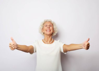 Yaşam tarzı, duygu ve insan konsepti: Yaşlı mutlu kadın başparmağını kaldırıyor ve kameraya bakıyor