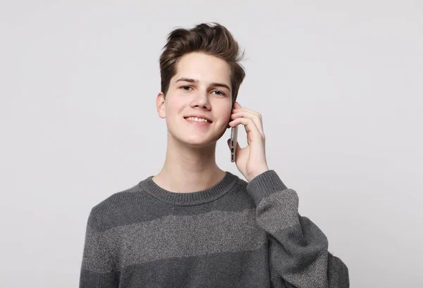 Smiling man in t-shirt talking by smartphone over grey background — Stock Photo, Image