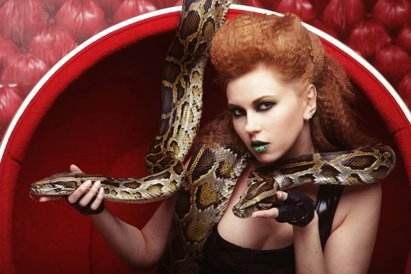 Mulher atraente em cadeira vermelha holdung python — Fotografia de Stock