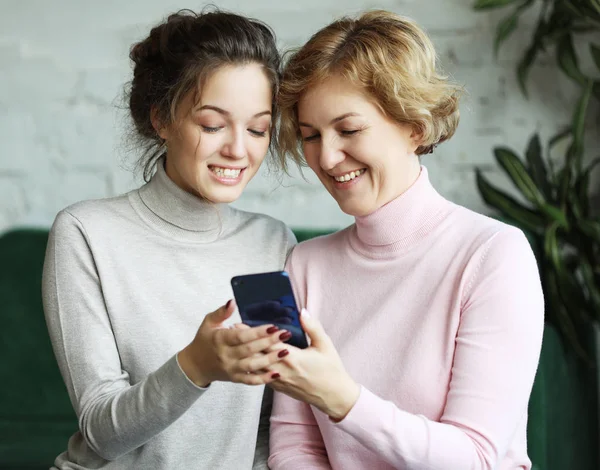 Сім'я, люди та концепція технології: у віці жінка та її доросла дочка використовують смартфон вдома — стокове фото