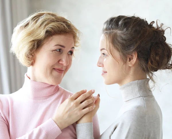 Beautiful senior mom and her adult daughter are hugging, looking at camera and smiling. At Home — Stock Photo, Image