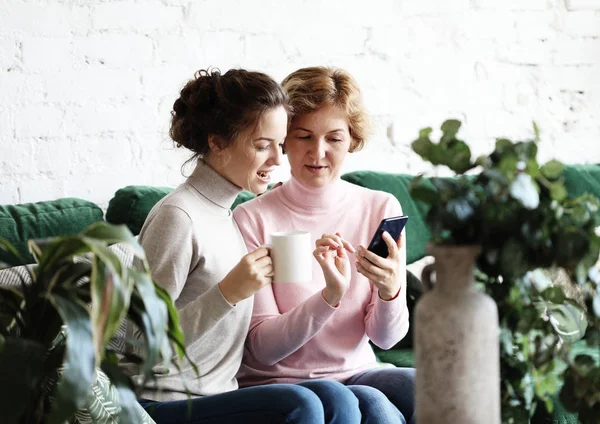 Conceito de família, pessoas e tecnologia: mulher idosa e sua filha adulta usando smartphone em casa — Fotografia de Stock