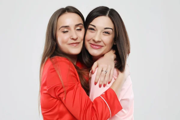 Estilo de vida, la amistad y el concepto de la gente - dos hermosas chicas vestidas en pijama abrazando y sonriendo — Foto de Stock