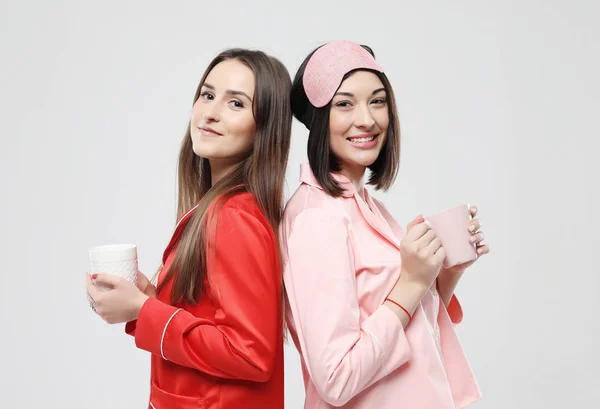 Zwei schöne Mädchen im Pyjama umarmen und halten Tassen — Stockfoto
