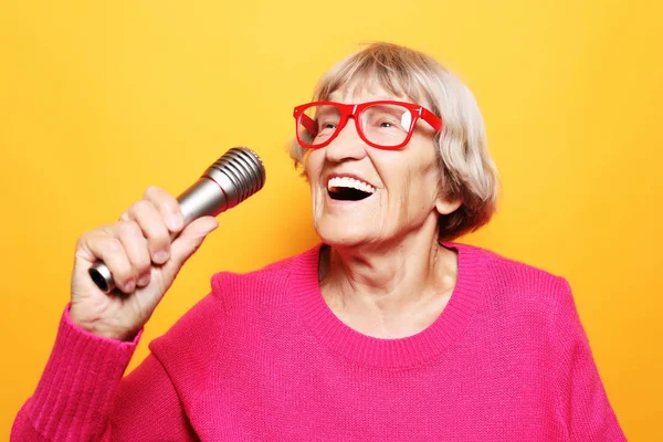 Retrato de la abuela divertida sostiene el soporte del micrófono y canta aislado sobre fondo amarillo vivo — Foto de Stock