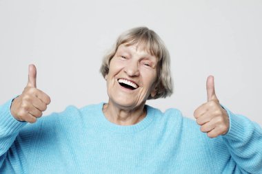 Yaşlı kadın başparmağını kaldırıyor ve kameraya bakıyor. 