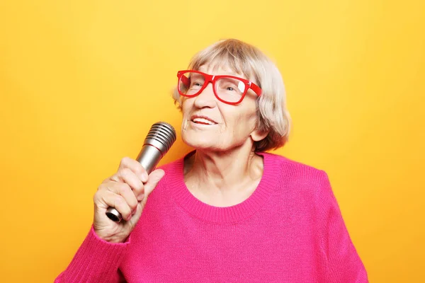Styl życia i koncepcja ludzi: Portret zabawnej babci trzyma stojak na mikrofon i śpiewa — Zdjęcie stockowe