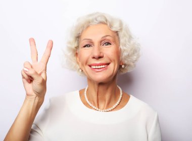 Yaşlı kadın gülüyor ve barış ya da zafer işareti gösteriyor. Duygular ve duygular. Anlamlı büyükannenin portresi..