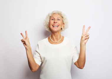 Yaşlı kadın gülüyor ve barış ya da zafer işareti gösteriyor. Duygular ve duygular. Anlamlı büyükannenin portresi..