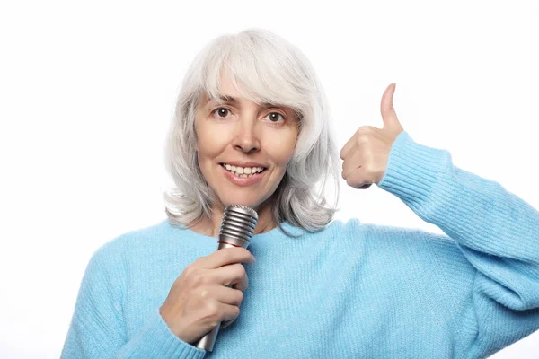 Életmód, érzelem és emberek koncepció: boldog idős nő énekel mikrofonnal, szórakozás, kifejező zenei tehetség fehér háttér — Stock Fotó