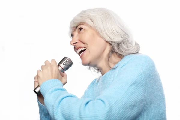 Styl życia, emocje i koncepcja ludzi: Szczęśliwa staruszka śpiewająca z mikrofonem, bawiąca się, wyrażająca talent muzyczny na białym tle — Zdjęcie stockowe