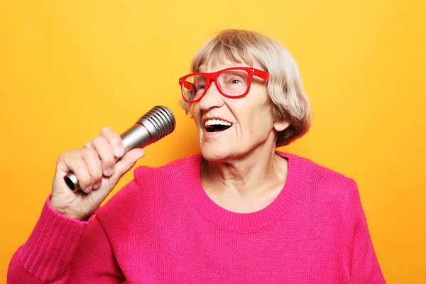 Estilo de vida y el concepto de la gente: Retrato de la abuela divertida sostiene el soporte del micrófono y canta aislado sobre fondo amarillo vivo — Foto de Stock