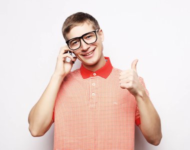 Cep telefonuyla konuşurken jest yapan ve gülümseyen tişörtlü genç adam.