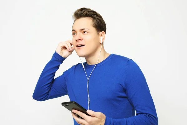 Feliz joven y elegante hombre ajustando sus auriculares y sonriendo mientras está de pie sobre fondo blanco — Foto de Stock