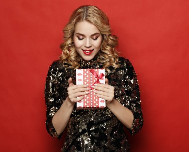 Kırmızı arka planda izole edilmiş hediye kutusunu tutan mutlu bir kadının portresi.