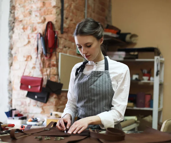 Mujer joven trabaja en un estudio de fabricación de bolsas, corta detalles — Foto de Stock