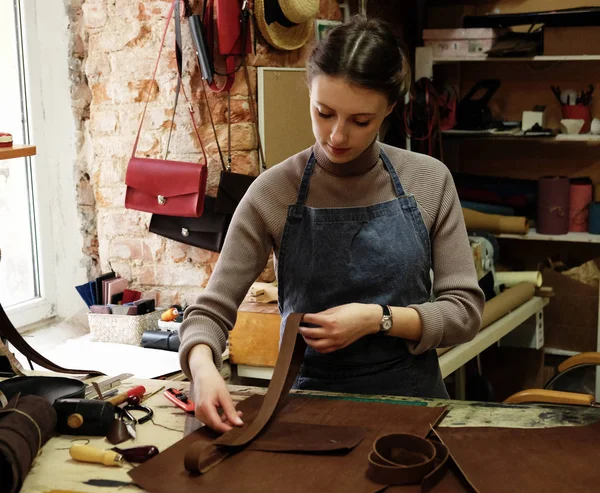 Young woman works in a bag making studio, cuts out details — Stock Photo, Image