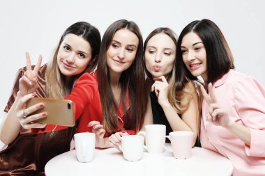 Pijama dört güzel kız masada oturuyor, çay veya kahve içme ve bir sosyal ağda sohbet.