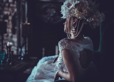 Beyaz elbise giyen güzel genç gelin ve çiçekler çelenk bir sandalyeye oturur. Lüks Saray.