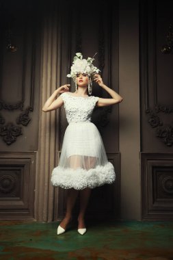 Beyaz elbise ve saray odasında ayakta çiçekler çelenk giyen genç güzel kadın.